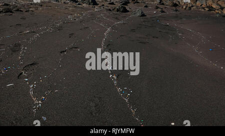Plastic particles washed up by the waves on a beautiful black sand beach, damaging effect of human pollution, impacting the environment Stock Photo