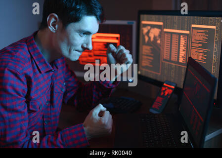 Male hacker celebrates success with a hand gesture. A successful attempt at system hacking and data theft. The concept of cybersecurity Stock Photo