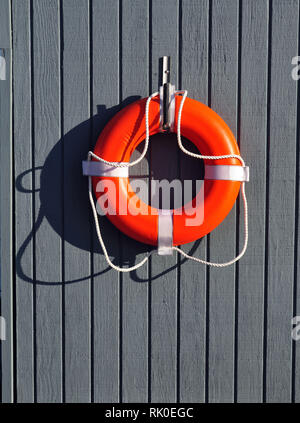 An Orange Life Buoy hanging on a grey wall of a boathouse Stock Photo