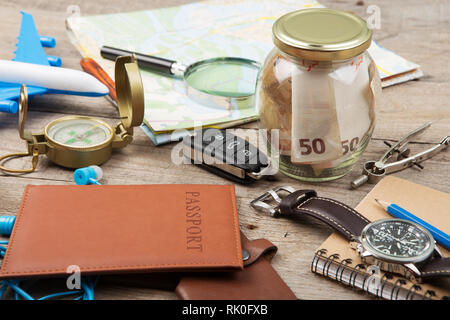 Jar with money for a travel, airplane, maps, passport, and other stuff for adventure on the table Stock Photo