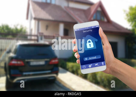 Smartphone with home security app in a hand on the building background Stock Photo
