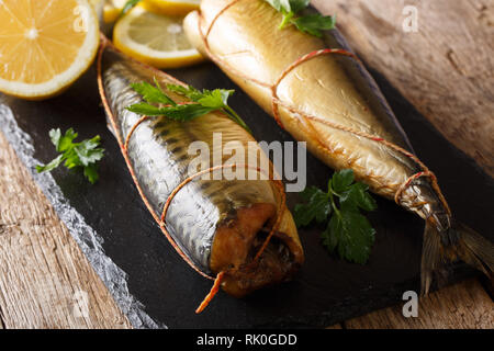 Smoked mackerel with lemons and parsley closeup on a black slate board on the table. horizontal Stock Photo