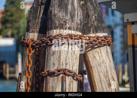 Pier wooden poles tightened together by rusty chains on canal in Venice, Italy. Stock Photo