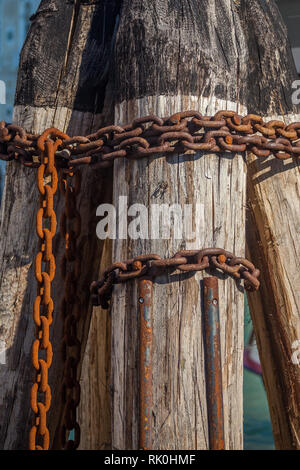 Pier wooden poles tightened together by rusty chains on canal in Venice, Italy. Stock Photo