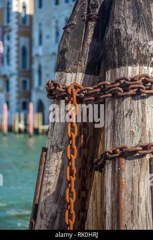 Pier wooden poles tightened together by rusty chains on canal in Venice, Italy. Stock Photo