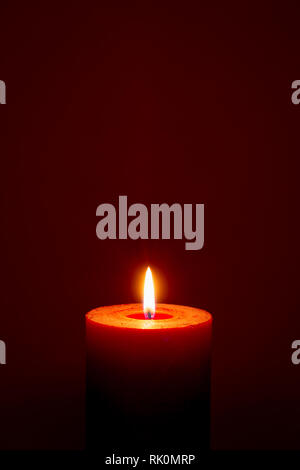 Single burning red candle on dark red background closeup Stock Photo