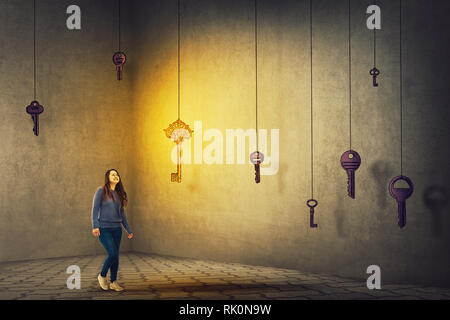 Confident young woman walking in a dark room to find the magic key to success. Concept of business aspirations, achievement and the right choice. Ambi Stock Photo