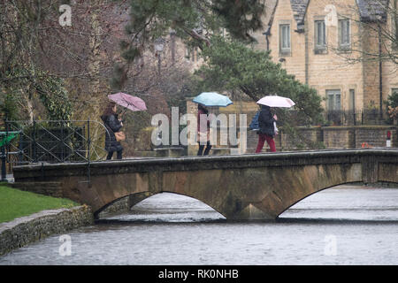 Tourists with their umbrellas as they cross a bridge during a rain shower on a wet and windy day in Bourton-on-the-Water in Gloucestershire. 08.02.19. Stock Photo