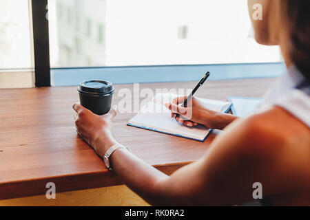 Unrecognizable freelance woman writing in notebook at cafe Stock Photo