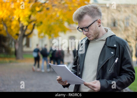 Pensive student in casual clothes is preparing to sign papers in his hand Stock Photo