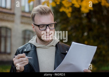 Portrait of a smiling student in casual clothes holding a pen with papers and looking at them Stock Photo