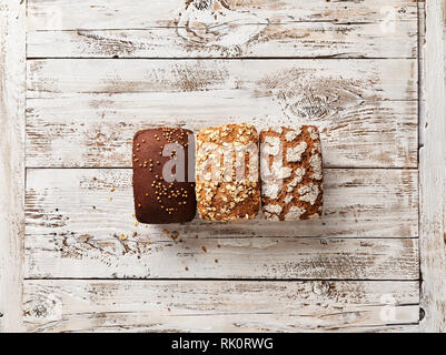 Three loaves of bread on white wooden background. Bakery concept with empty space for design. Gluten-free rye bread with bran and coriander Stock Photo