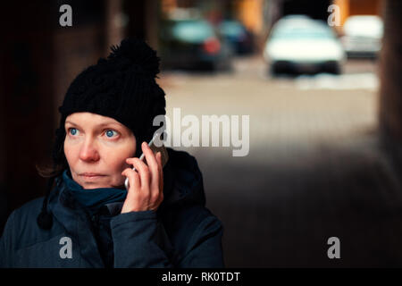 Concerned worried woman talking on mobile phone on street on cold winter day