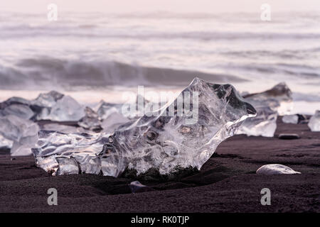 Striking ice formations on a black lava sand beach are highlighted by the evening light with red shades, narrow focus zone, depth effect, in the backg Stock Photo