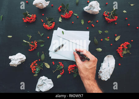 Hand writing on white blank envelope mock up copy space over dark desktop background decorated with wild berry fruit arrangement Stock Photo
