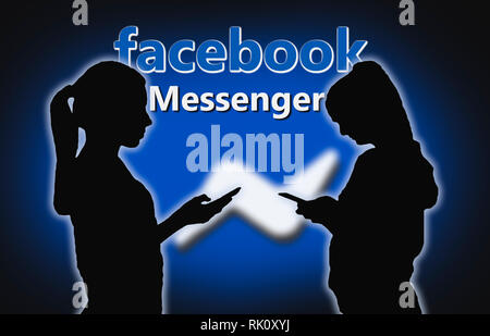 Silhouettes of a couple of young women facing each other using Facebook Messenger on smartphones. People using Messenger. Stock Photo