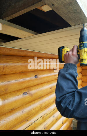 The worker works with a screwdriver, on the background of plastic and wooden round logs 2019 Stock Photo