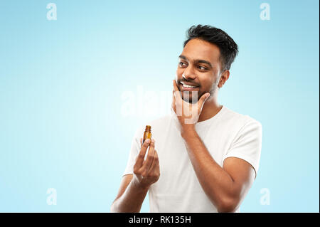 smiling indian man applying grooming oil to beard Stock Photo