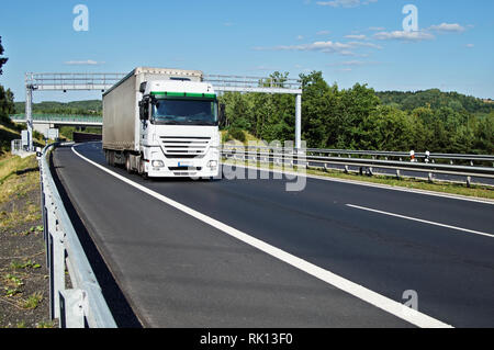 White truck passing through the electronic toll gates on the asphalt highway in a wooded landscape. Bridge and forested mountains in the background. W Stock Photo