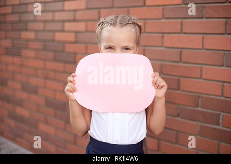 Close-up portrait of a young girl holding a blank sign on red brick wall background Stock Photo