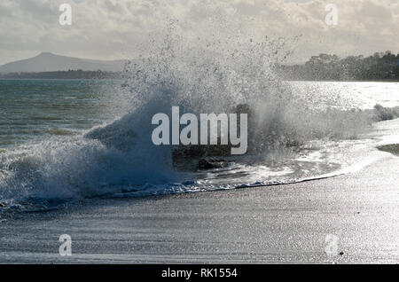Waves crash onto rocks on killiney beach,Dublin,Ireland,illuminated by the sun,driven by powerful onshore winds. Stock Photo