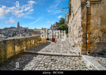 Typical forked hillside path with a red door near the Convent of Saint Agostino in the ancient city of Matera, Italy, with the church tower visible in Stock Photo