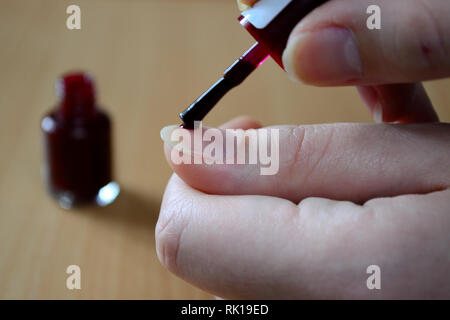 Female hands doing nails with blood red colored polish Stock Photo