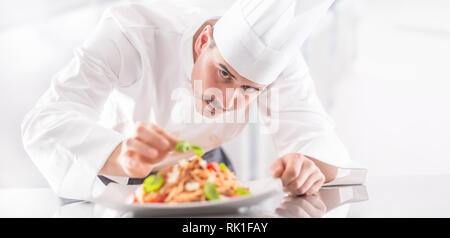 Chef in restaurant kitchen prepares and decorates meal with hands. Cook preparing spaghetti bolognese. Stock Photo