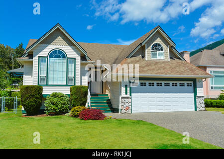 Suburban house in British Columbia for sale. Big house with wide garage door, concrete driveway, and lawn in front for sale. House with mountain view  Stock Photo