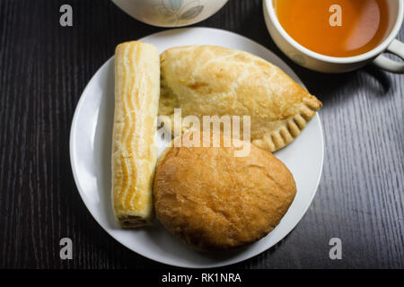 Tea and Pastries - Overhead shot of a white plate of assorted pastries with  a partial view of a teapot and teacup on a black tabletop Stock Photo