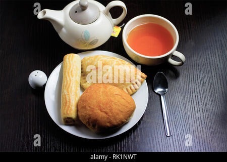 Tea and Pastries - Overhead shot with a white plate with assorted pastries, a teapot and teacup on a black tabletop Stock Photo
