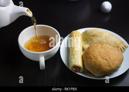 Tea and Pastries - Overhead shot with a white plate filled with assorted pastries and  a teapot pouring tea into a cup Stock Photo