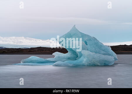 Glacier lagoon with a large blue iceberg in the foreground, mountains and a huge glacier in the background, light at the end of the day, water movemen Stock Photo