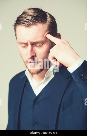 Young intellectual with closed eyes dealing with problem Portrait of tired businessman pressing his pointing finger on head isolated on gray Stock Photo