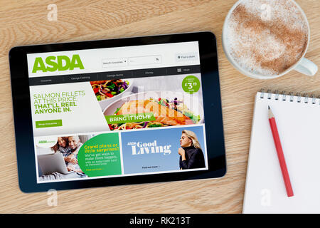 The Asda website features on an iPad tablet device which rests on a wooden table beside a notepad (Editorial use only). Stock Photo