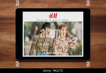 The website of H&M is seen on an iPad tablet, which is resting on a wooden table (Editorial use only). Stock Photo