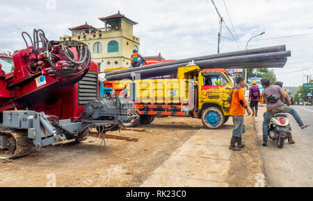 Workmen in a yard unloading pipes from a truck, and heavy equipment,  in Jimbaran, Bali Indonesia., Bali Indonesia. Stock Photo