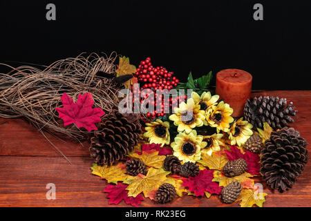 Silk maple leaves, beautiful bouquet of sunflowers, frosted pinecones and orange candle on tabletop with dark background. Stock Photo