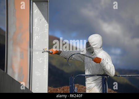 A tradesman spray paints steel beams with primer at a construction site Stock Photo