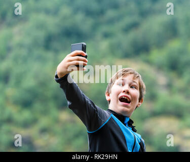 Candid portrait of young boy taking selfie using mobile phone outdoors Stock Photo