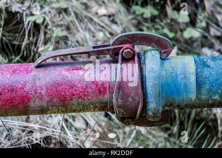 Coupling of red and blue pipe close-up. Old colored metal piping with clutch with blurred green grass in background. Cohesiveness and fixed connection. Stock Photo