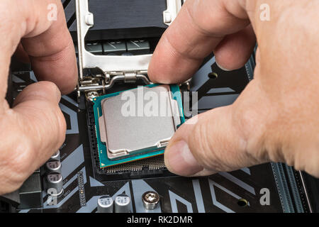 Detail of expert hands at processor replacement. Installation of central processing unit into a socket on computer mainboard. PC hardware maintenance. Stock Photo