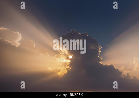 Beautiful nature background. Image of huge fluffy clouds hiding first morning sunlight. Straight sunrays shining behind cloud. Horizontal color photog Stock Photo