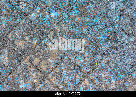Gray checked metallic texture with a rough uneven surface. Detail of chipped rusty iron cover of sewer. Relief pattern and traces of blue peeled paint. Stock Photo
