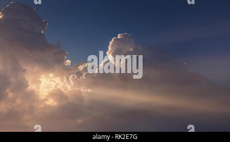 Beautiful nature background. Image of huge fluffy clouds hiding first morning sunlight. Straight sunrays shining behind cloud. Horizontal color photog Stock Photo