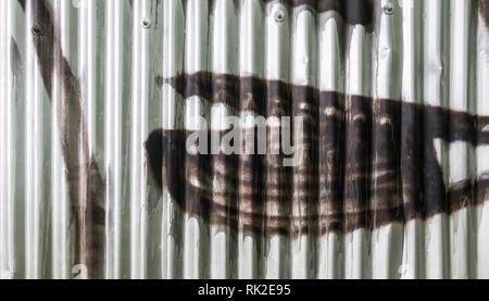Corrugated iron wall with graffiti detail as a background. Silvery fence. Wavy metal sheet sprayed by brown color. Close-up of pop art in city street. Stock Photo
