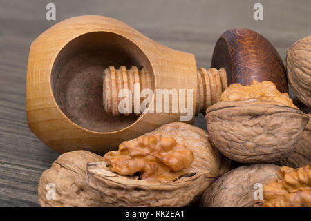Cracking of walnuts with a wooden screw nutcracker in mushroom shape. Close-up of the kitchen tool and a group of partly peeled nuts with half shells. Stock Photo