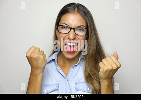 Happy successful young woman with raised hands shouting and celebrating success over gray background Stock Photo