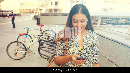 Portrait of an attractive young woman using a smartphone. Executive working with a mobile phone in the street. Panoramic banner view. Desatured retro  Stock Photo