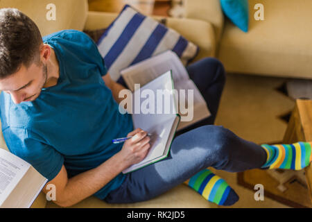 A young man is looking interested while taking notes from the books Stock Photo